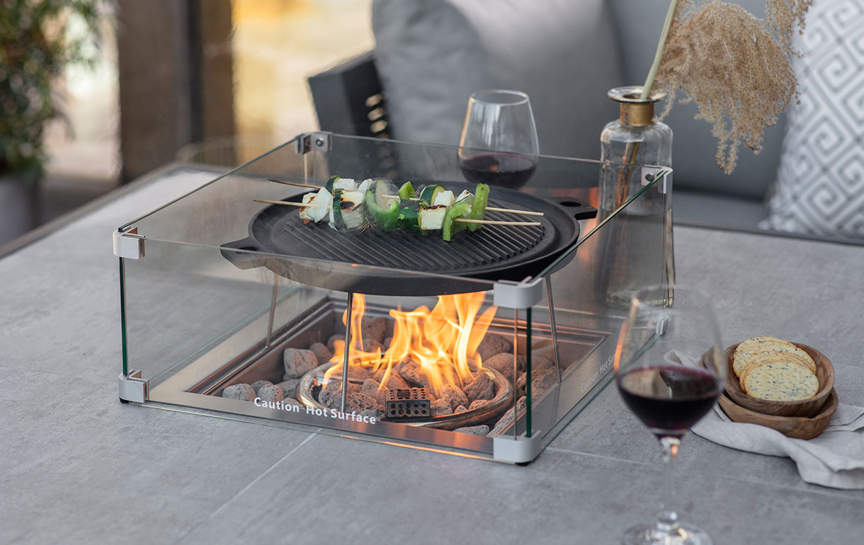 Gas firepit table with griddle cooking skewers