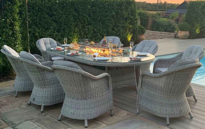 An oval grey rattan dining table with a built in gas firepit the table has eight dining chairs